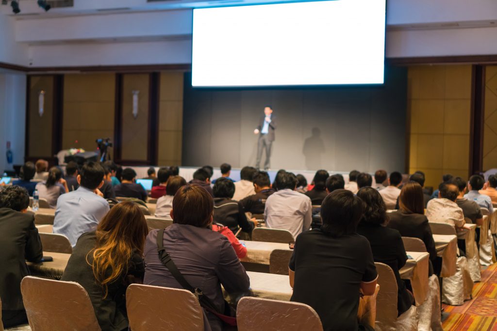 Rear side of Audiences sitting and listening the speackers on the stage in low light conference hall