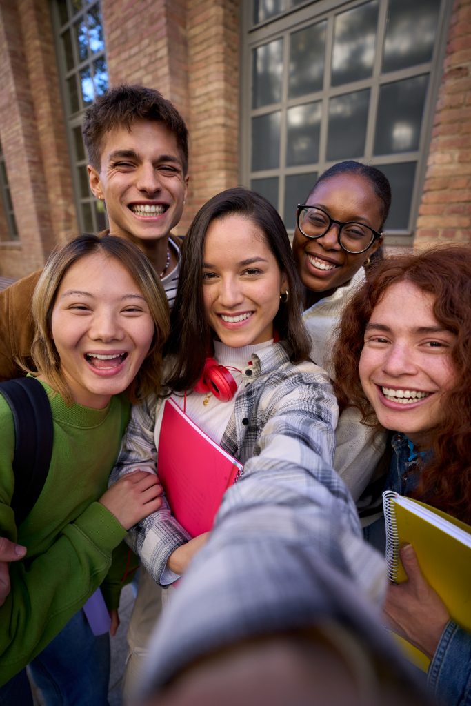 Vertical selfie of a Group of student happy multiracial friends having fun outdoors at university campus. Diverse cheerful joyful young people looking at camera and smiling and laughing together