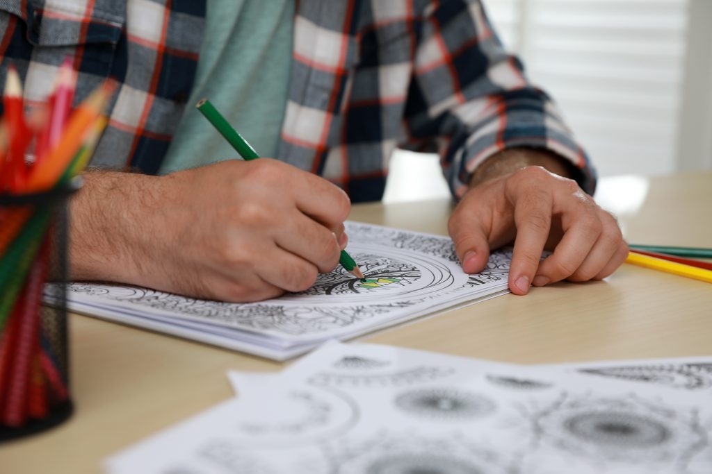 Man coloring antistress picture at table indoors, closeup