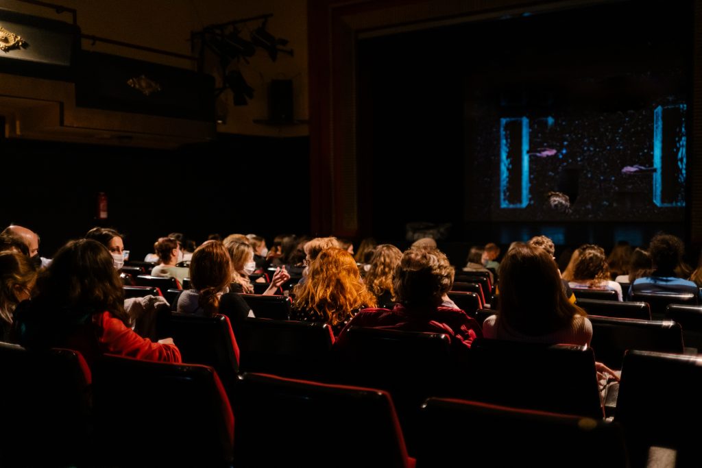 people with a mask watching a show in a theater maintaining sanitary measures